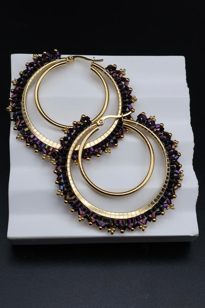 Gold hoop earrings with purple gemstones on a white platform