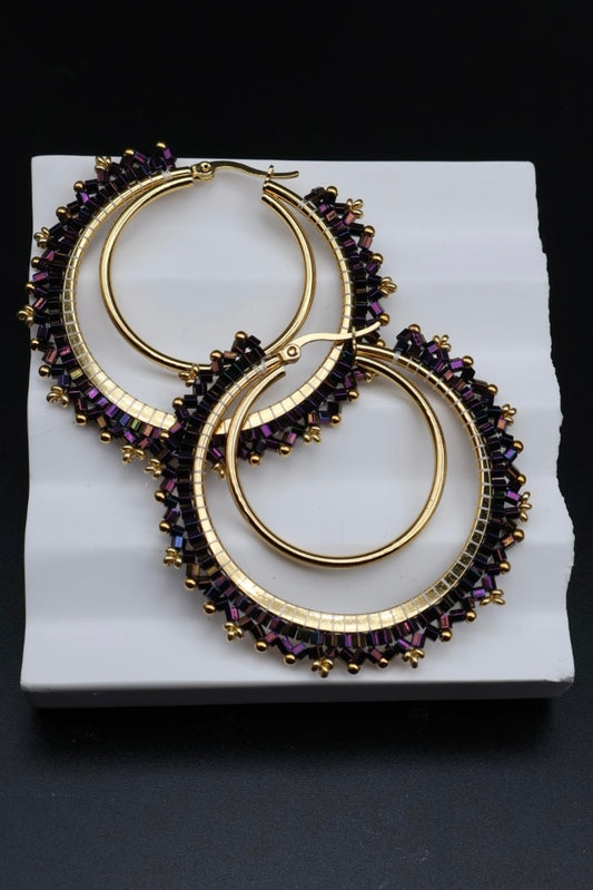Gold hoop earrings with purple gemstones on a white platform