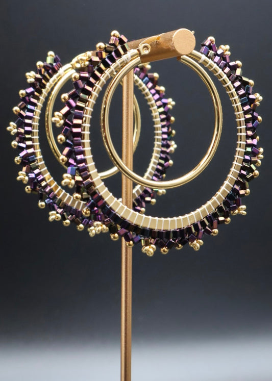Gold and purple beaded circular brooch on a dark background