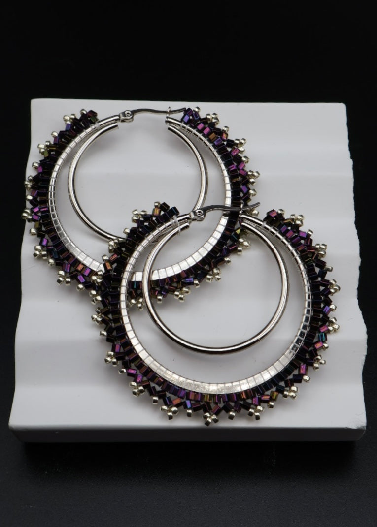 Pair of hoop earrings with purple gemstones on a white stand against a black background