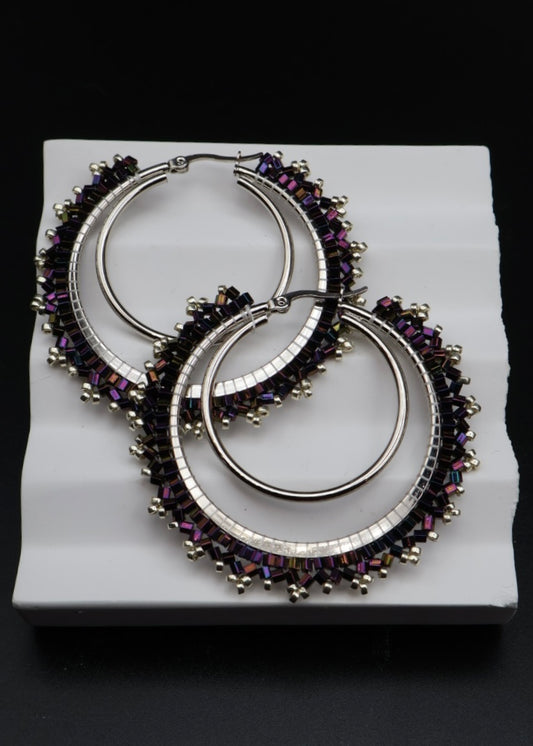 Pair of hoop earrings with purple gemstones on a white stand against a black background