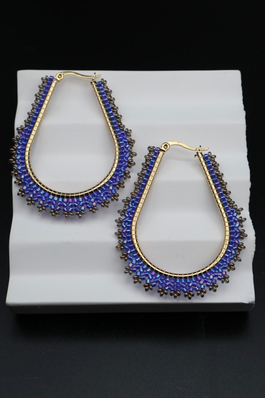 Pair of blue beaded earrings on a white stand with a black background