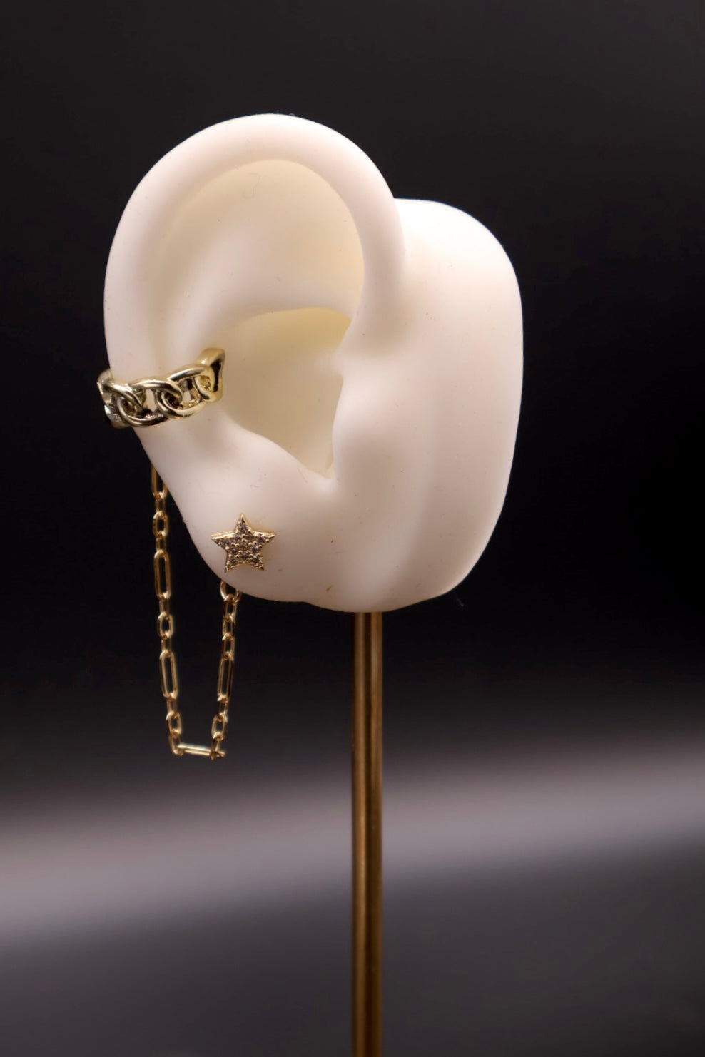 Gold chain earring on a white ear model with a dark background