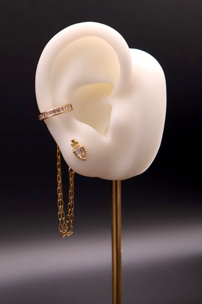 Gold earring displayed on a white ear model against a dark background