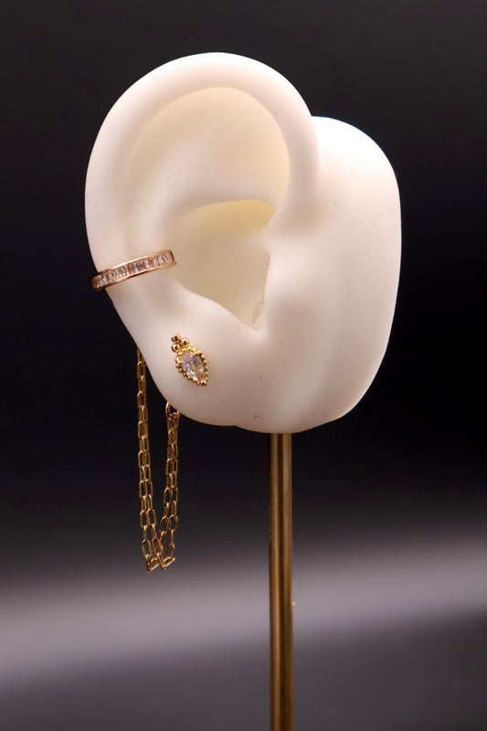 Gold earring displayed on a white ear model against a dark background