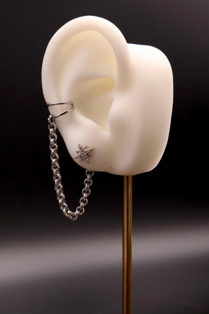 Silver chain earring on a white ear model against a black background