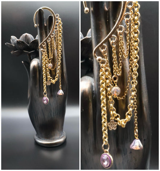 Gold chain earrings with pink gemstones on a black hand-shaped stand.