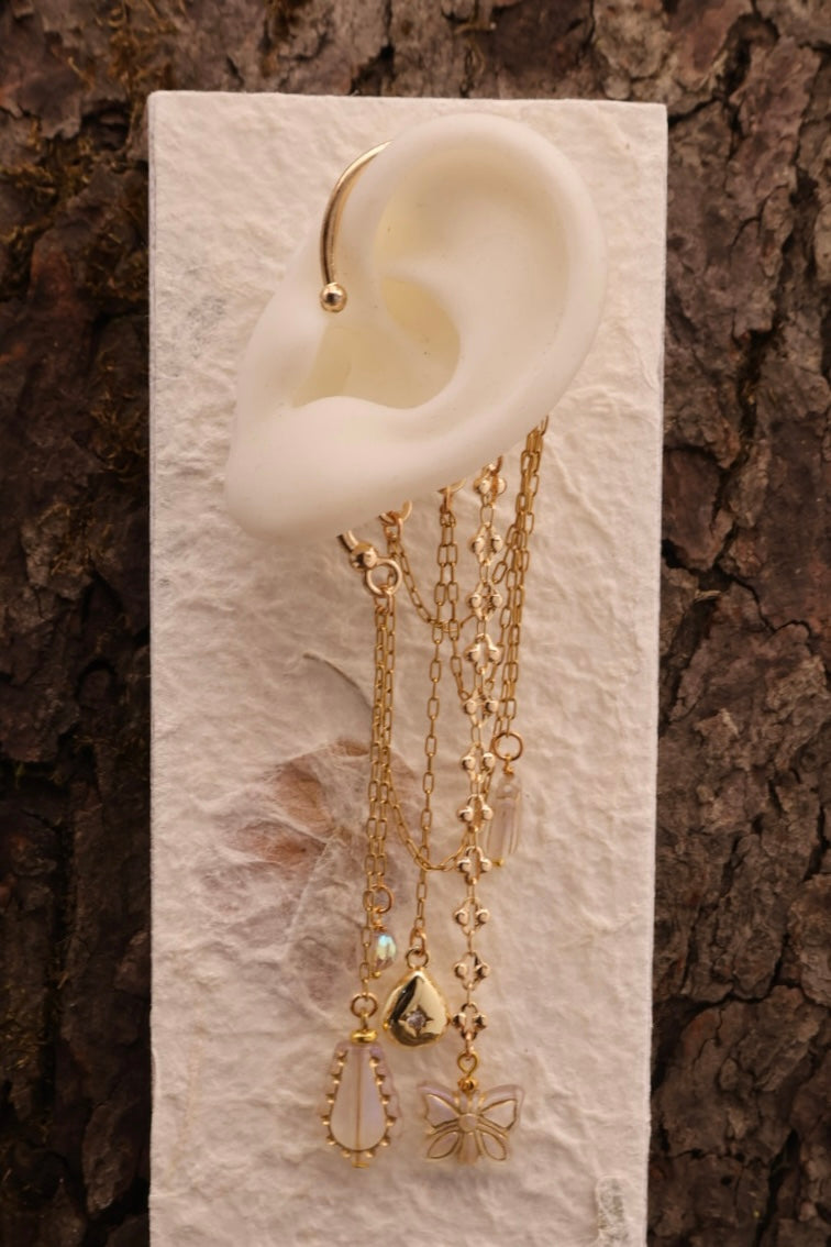 Gold earrings displayed on a white ear model against a textured brown background