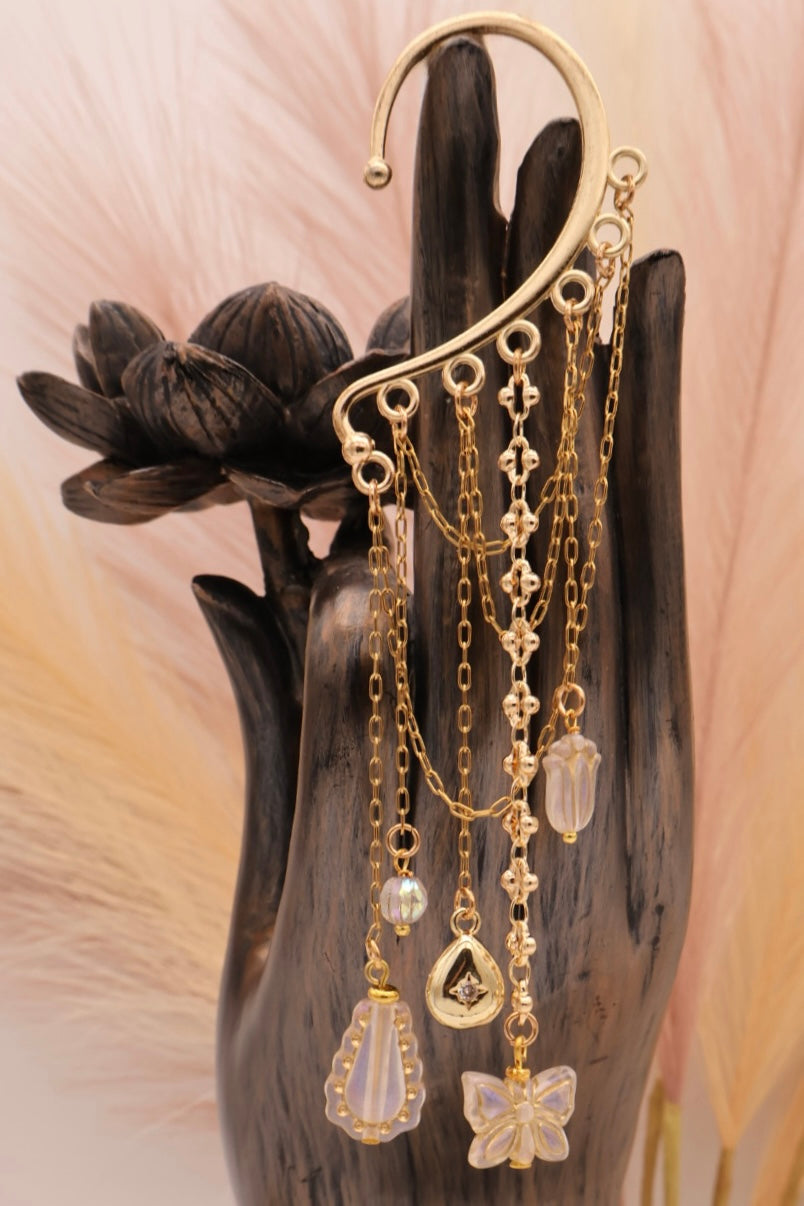 Gold earrings with chains and crystals on a dark hand holding a black flower.