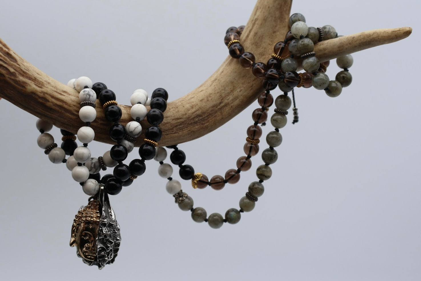 Three beaded necklaces with pendants on a branch against a gray background