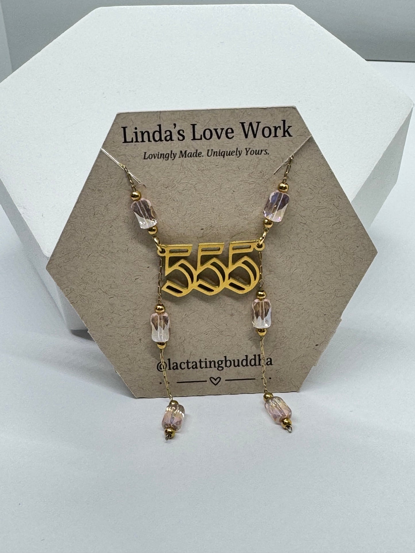 Necklace with gold pendant and clear beads on a branded card against a white background