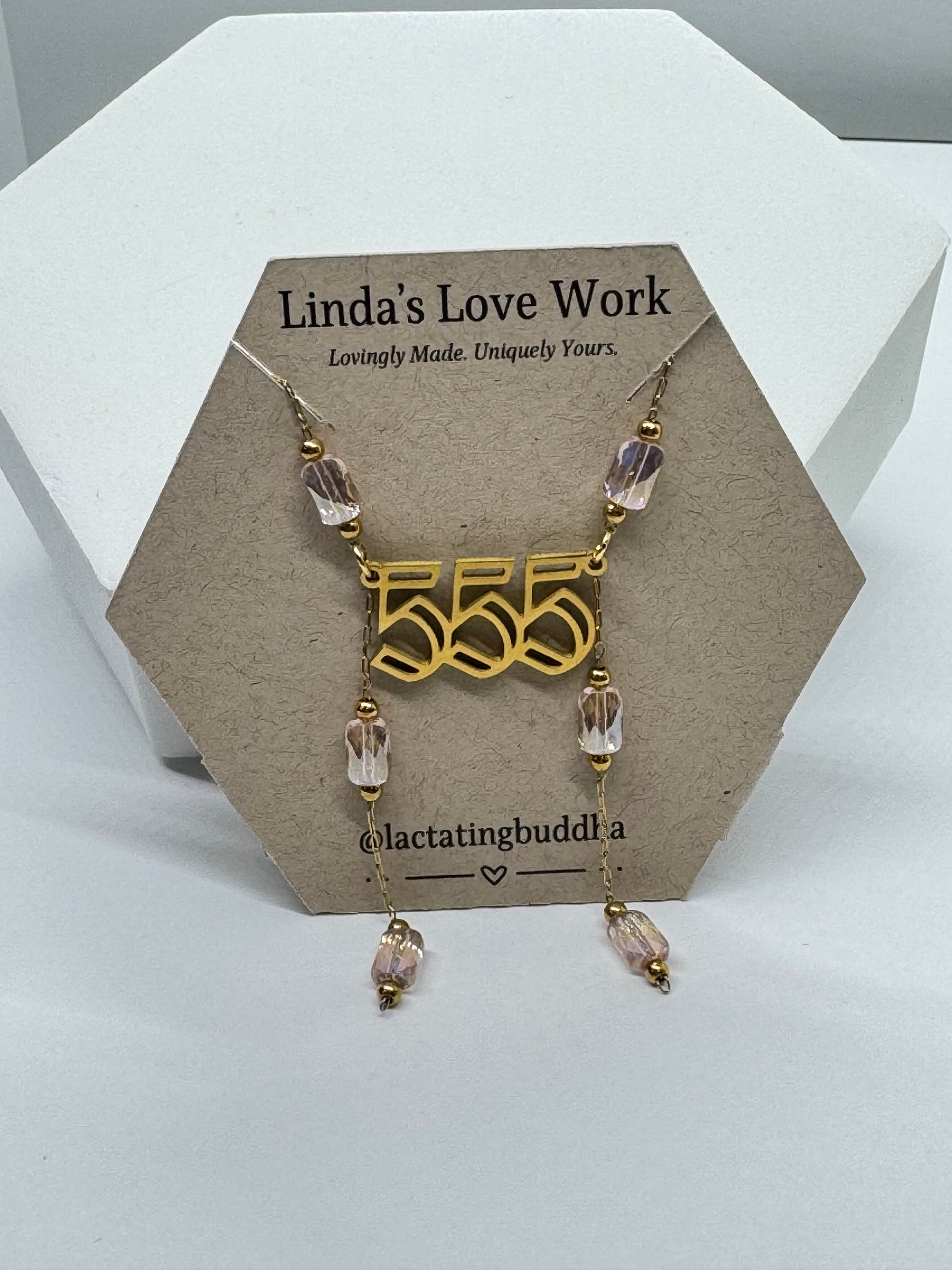 Necklace with gold pendant and clear beads on a branded card against a white background