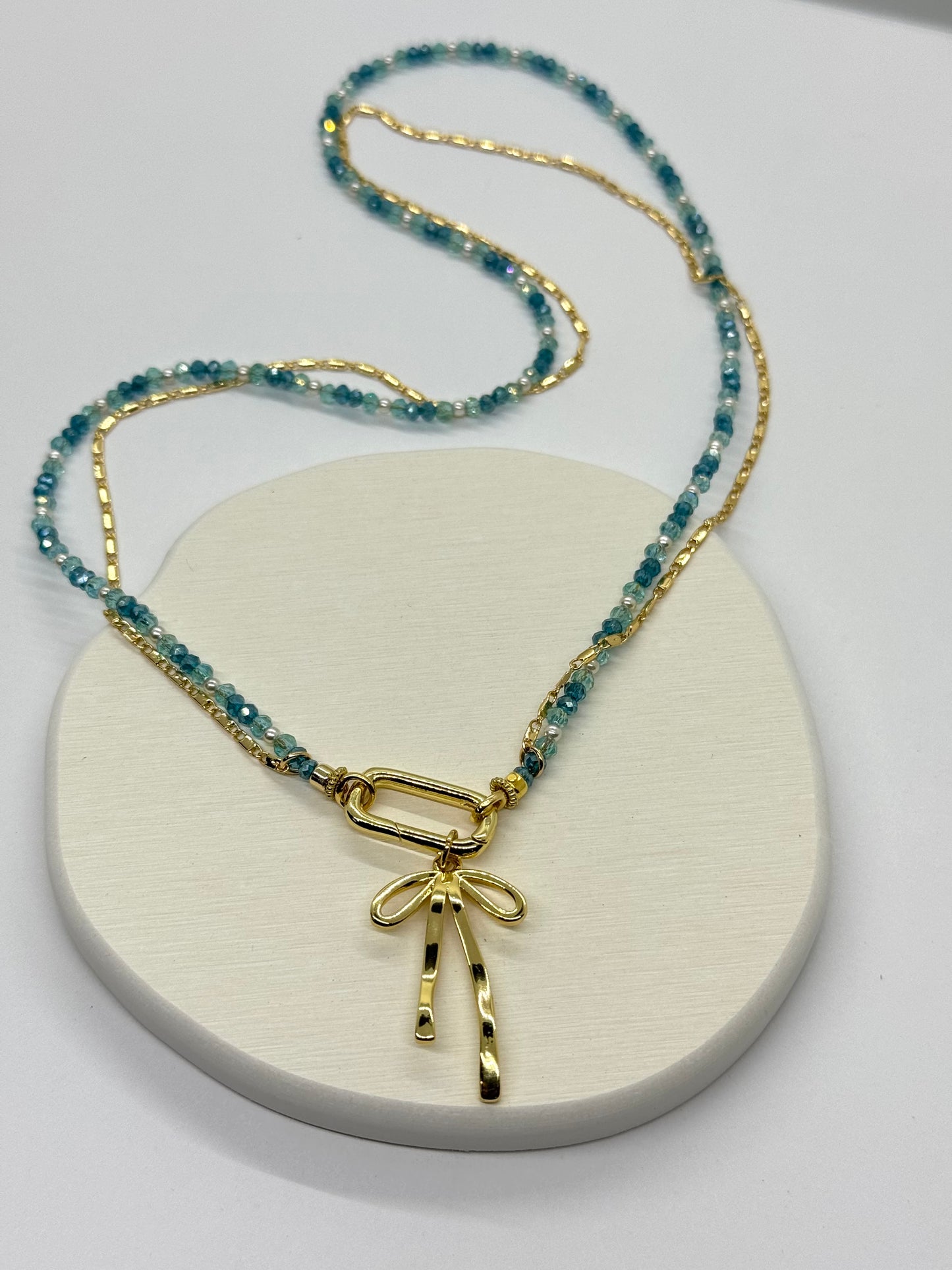 Necklace with blue beads and gold bow pendant on a white surface