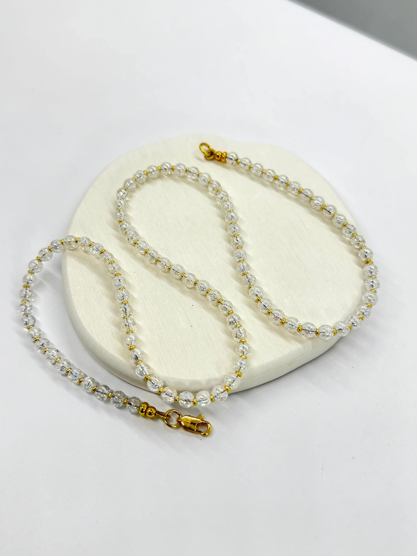 Gold and crystal necklace on a white stone surface