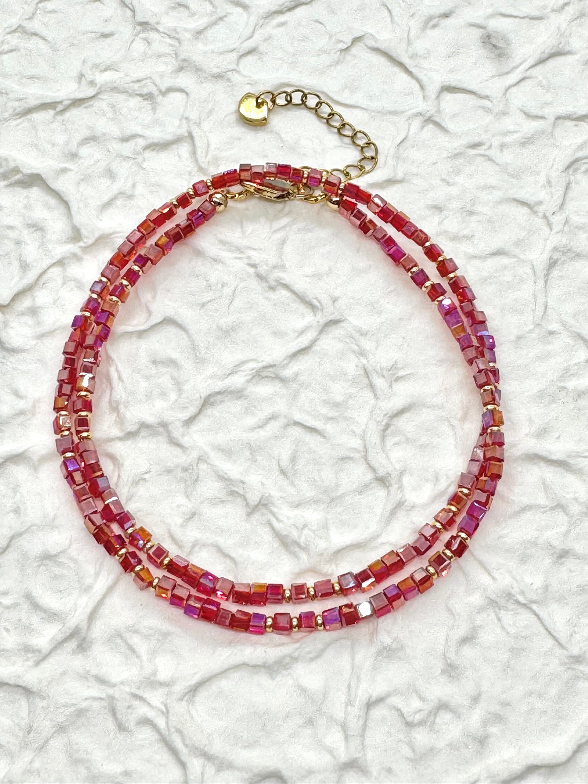A beaded necklace with red hues on a textured white background