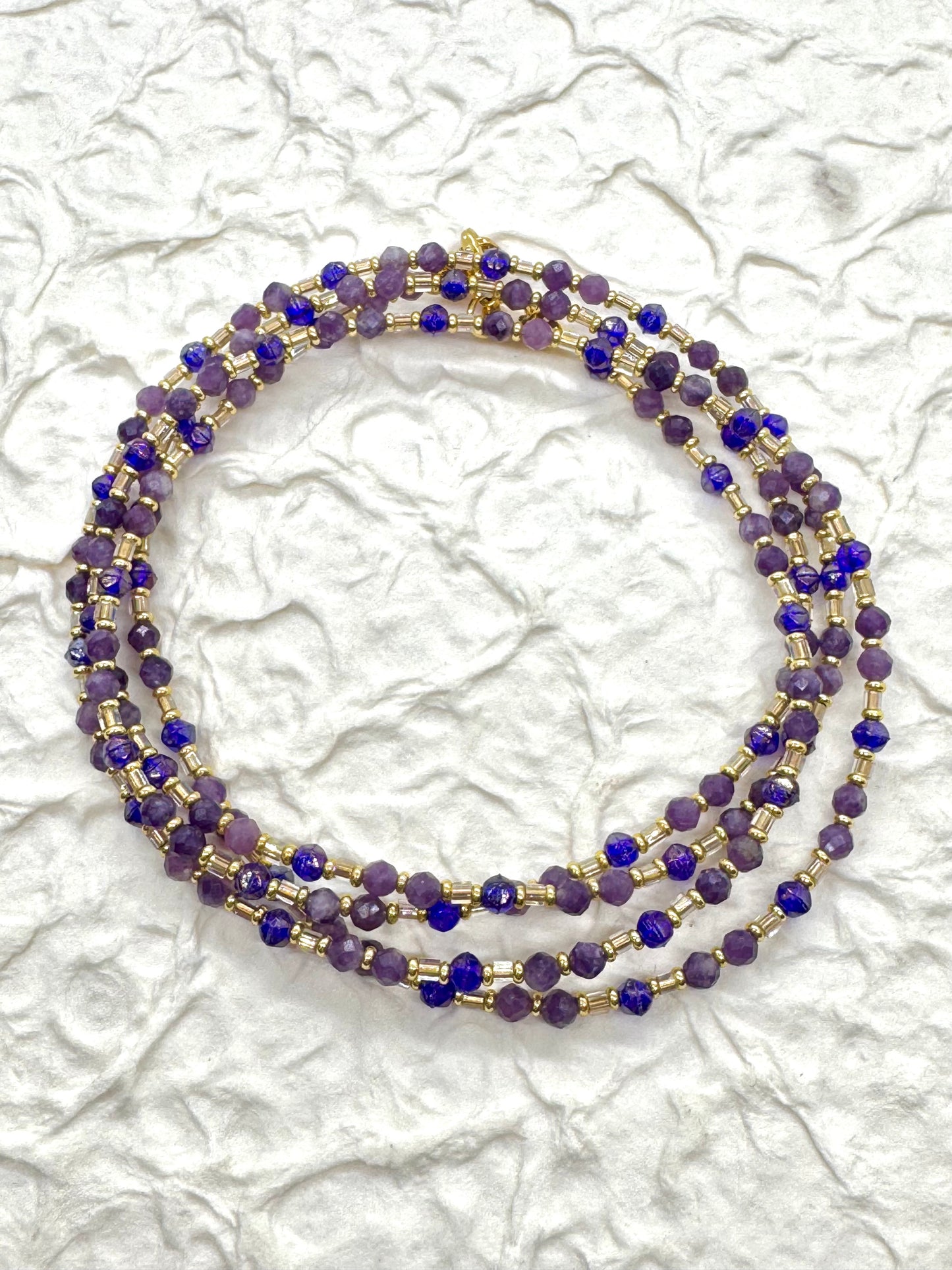 A beaded necklace with purple and gold accents on a textured white background