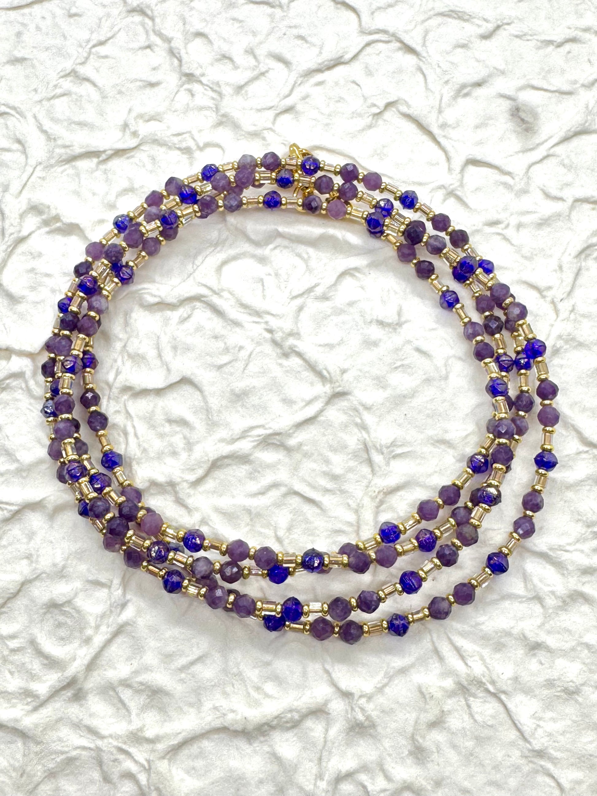 A beaded necklace with purple and gold accents on a textured white background