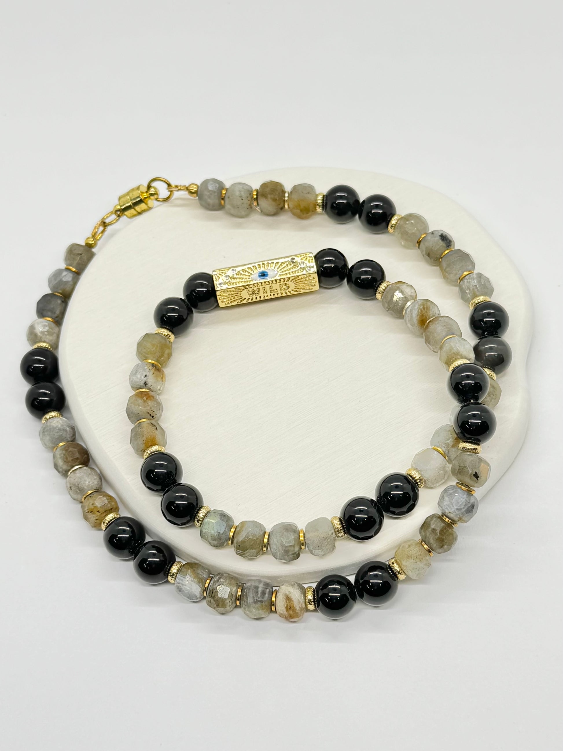 A beaded necklace with black and gray stones on a white surface