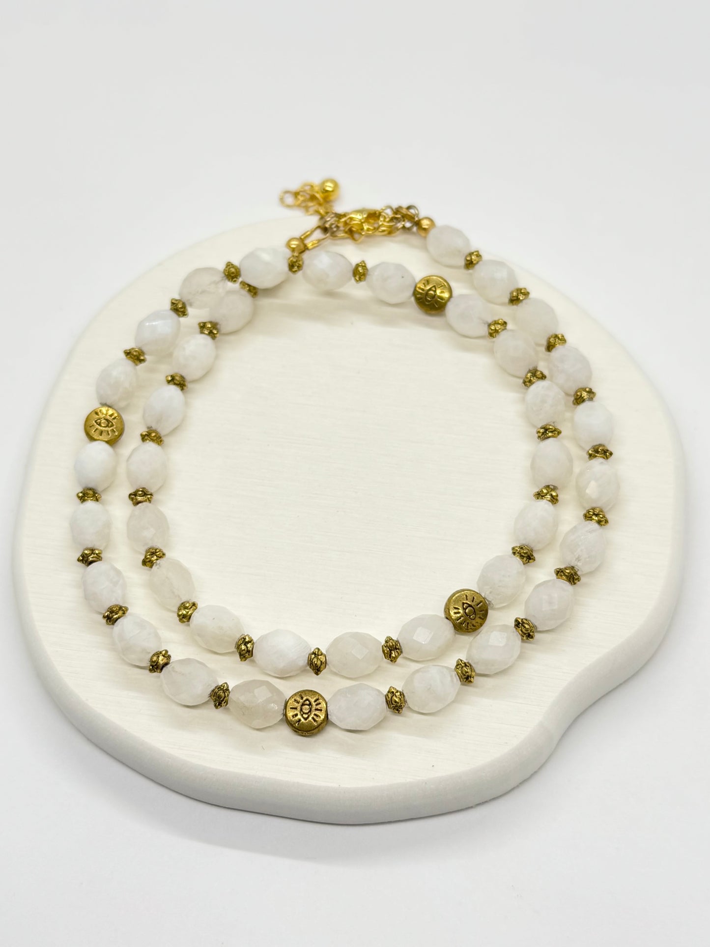 A white beaded necklace with gold accents on a white stand.
