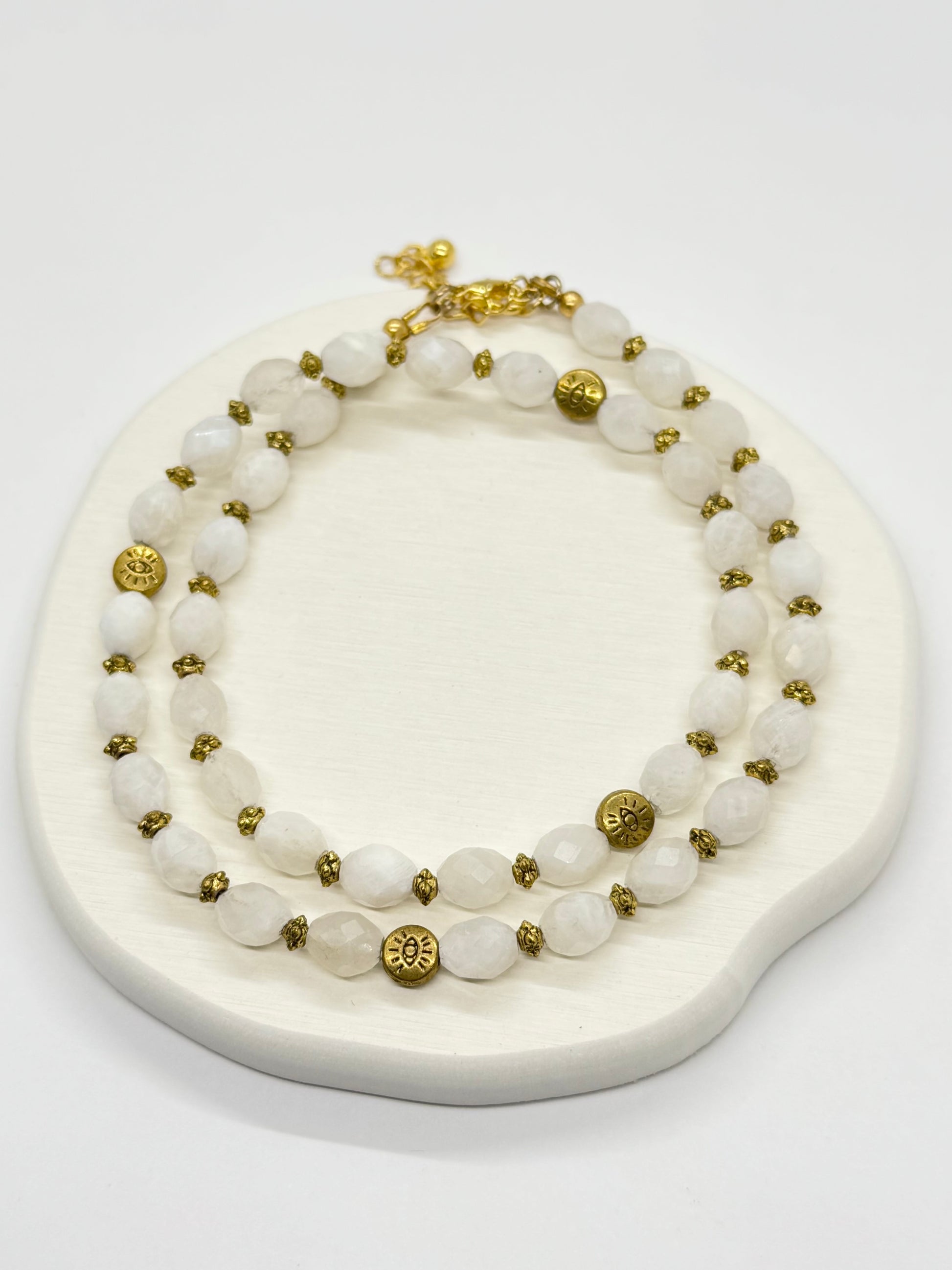A white beaded necklace with gold accents on a white stand.