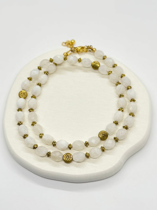 A white beaded necklace with gold accents on a white stand.