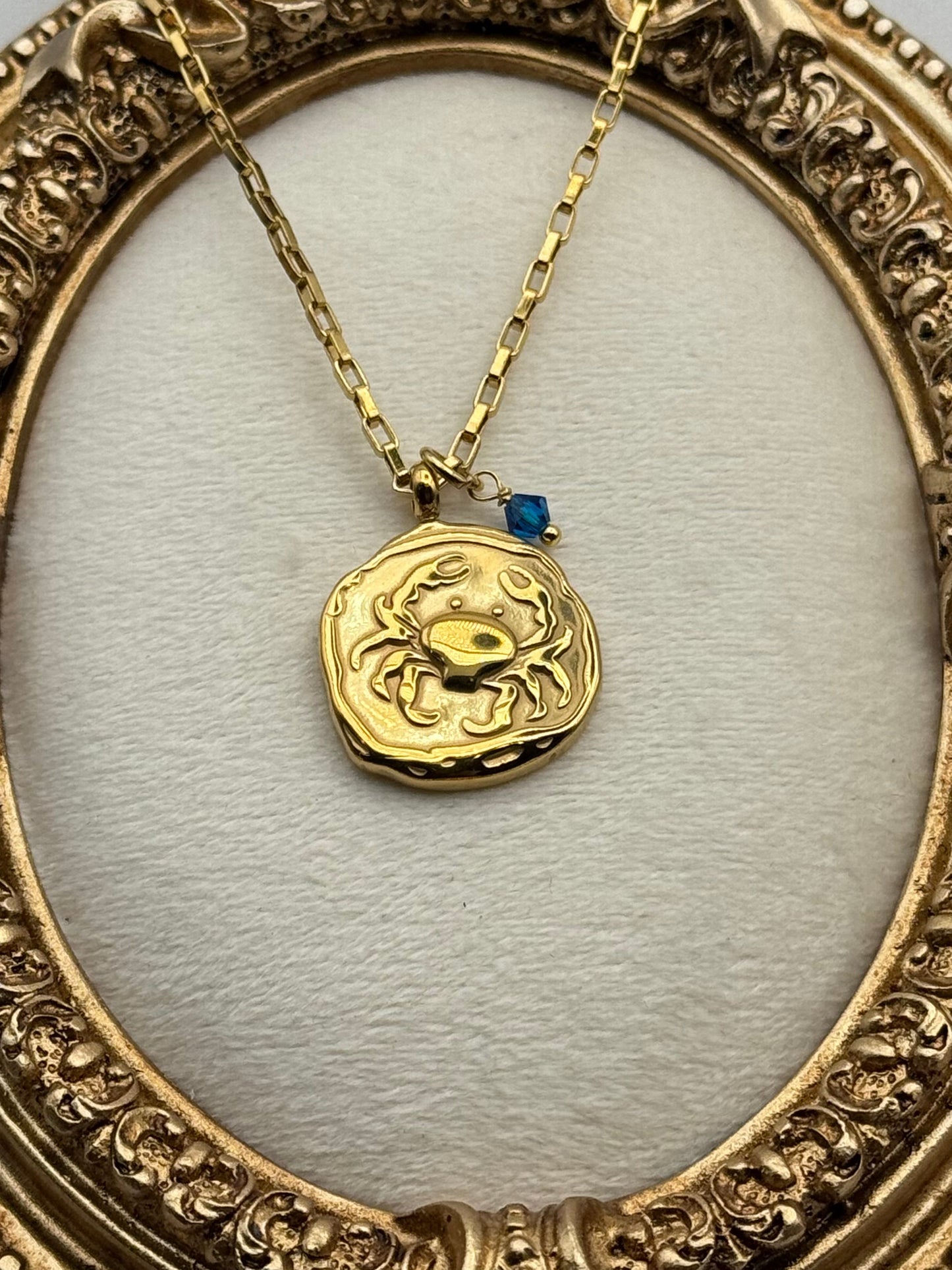 Gold necklace with a crab pendant in an ornate gold frame