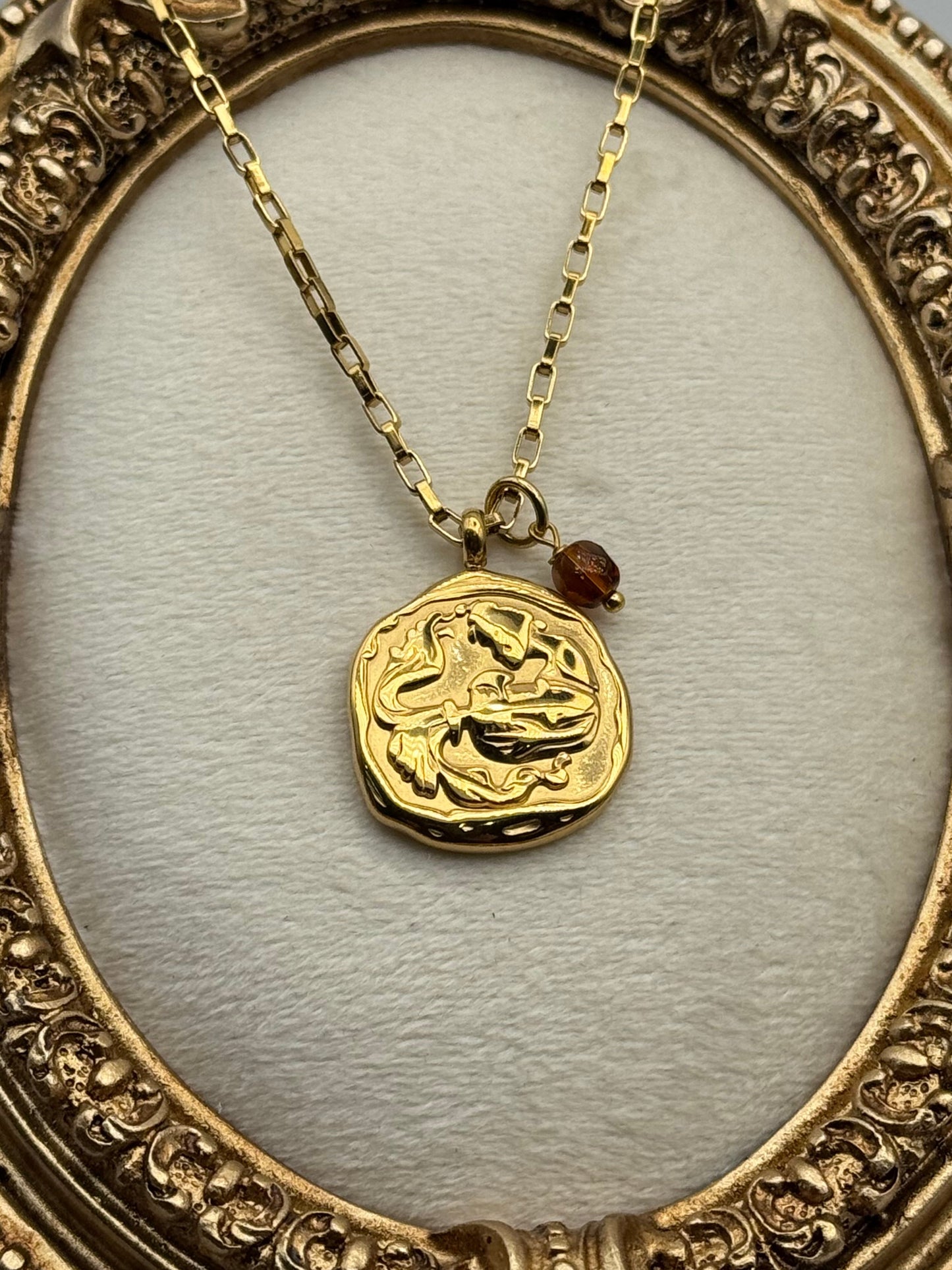Gold necklace with a decorative pendant in an ornate gold frame.
