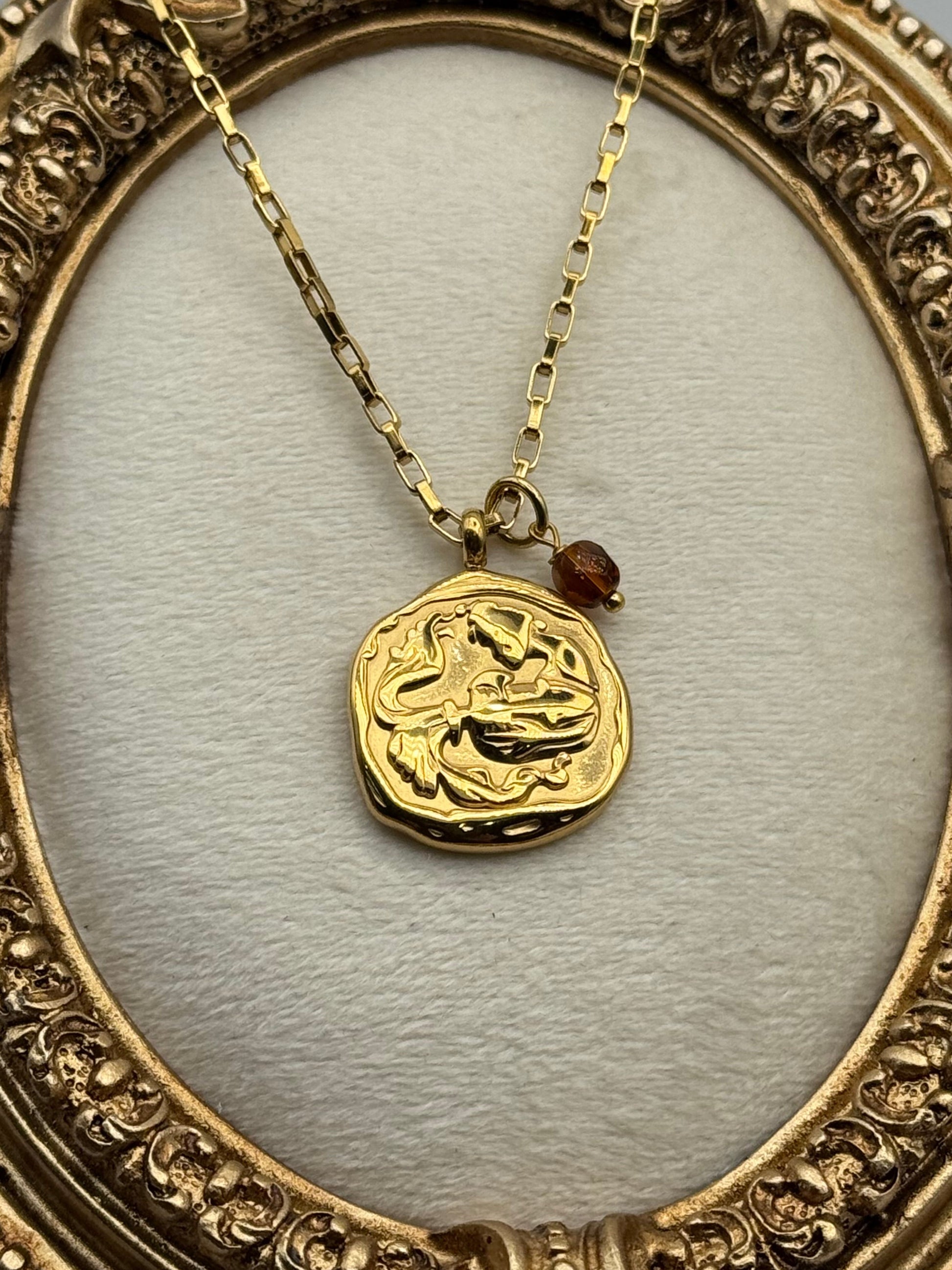 Gold necklace with a decorative pendant in an ornate gold frame.