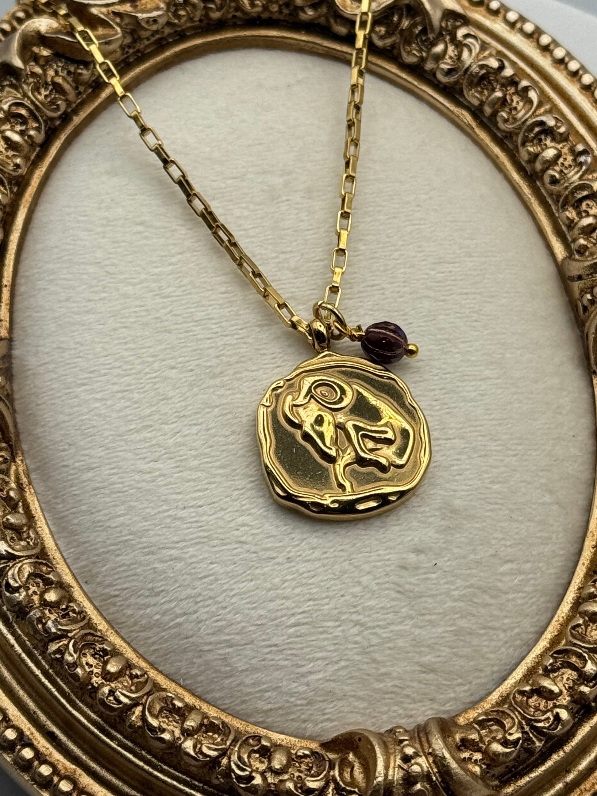 Gold necklace with a decorative pendant in an ornate gold frame.
