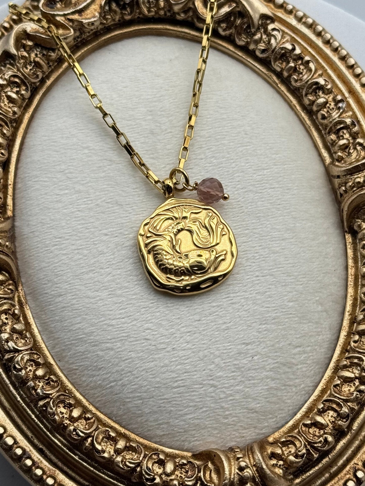Gold necklace with a round pendant on an ornate gold frame.
