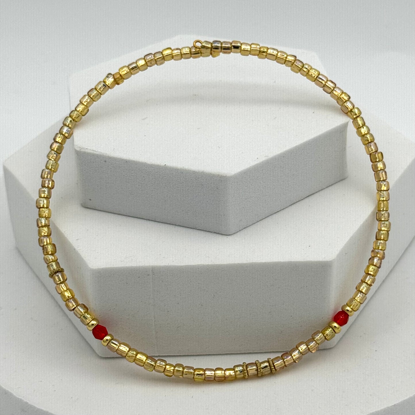 Gold beaded necklace with red accents on a white stand