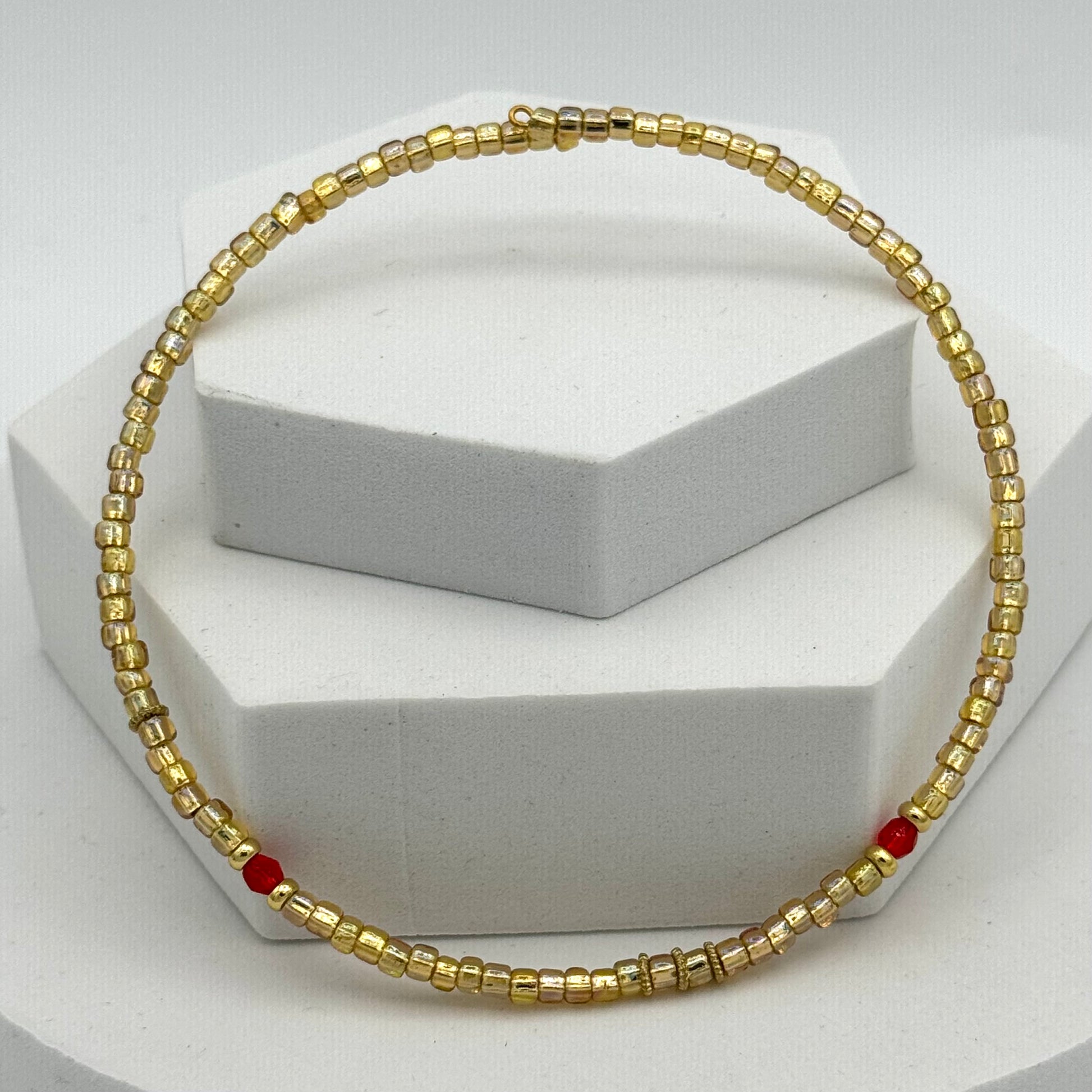 Gold beaded necklace with red accents on a white stand