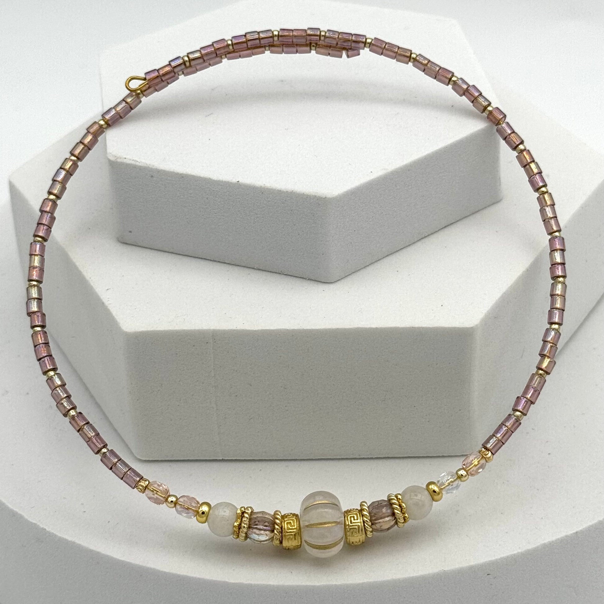 Necklace with pink and gold beads on a white stand