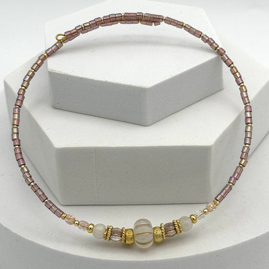 Necklace with pink and gold beads on a white stand