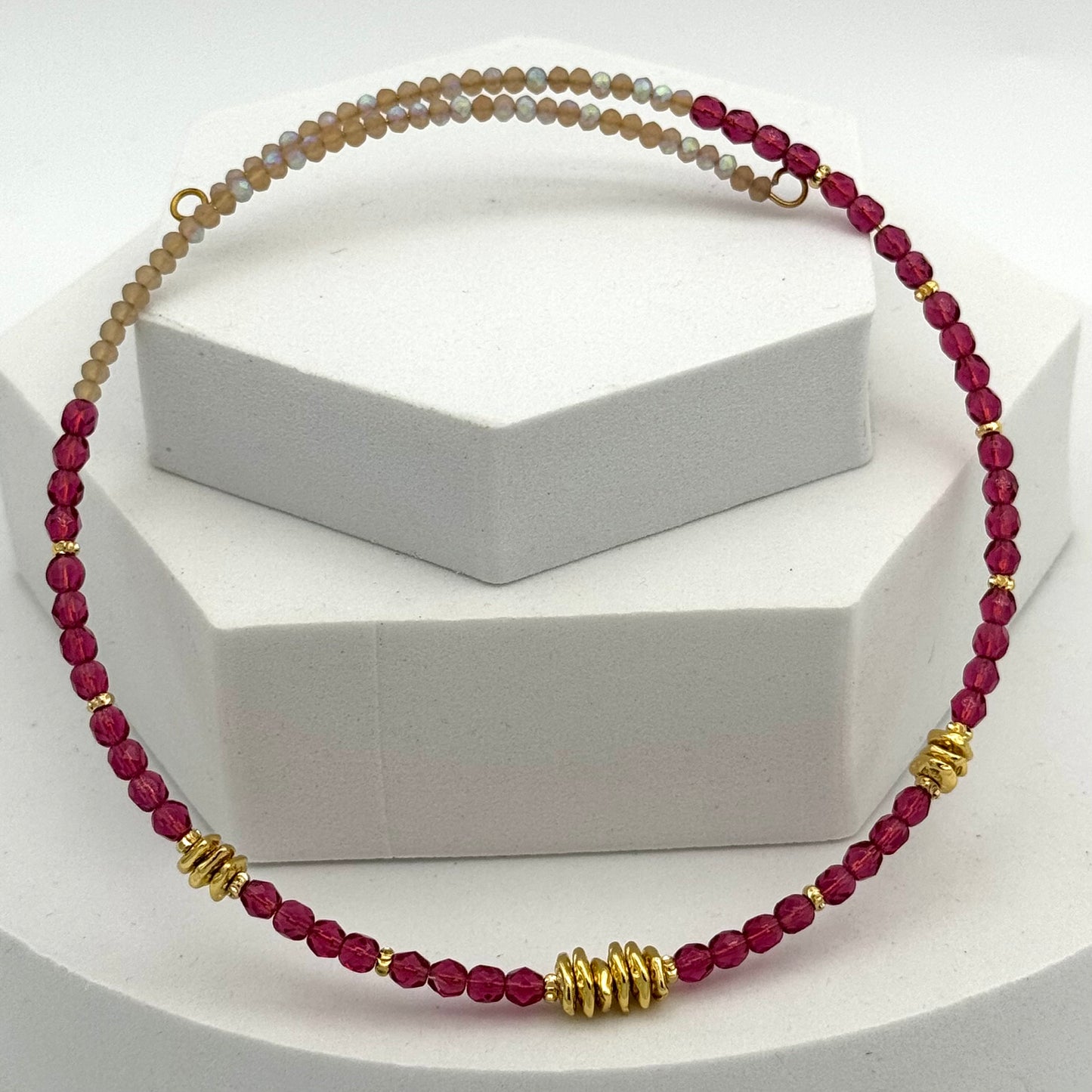 Necklace with red beads and gold accents on a white stand