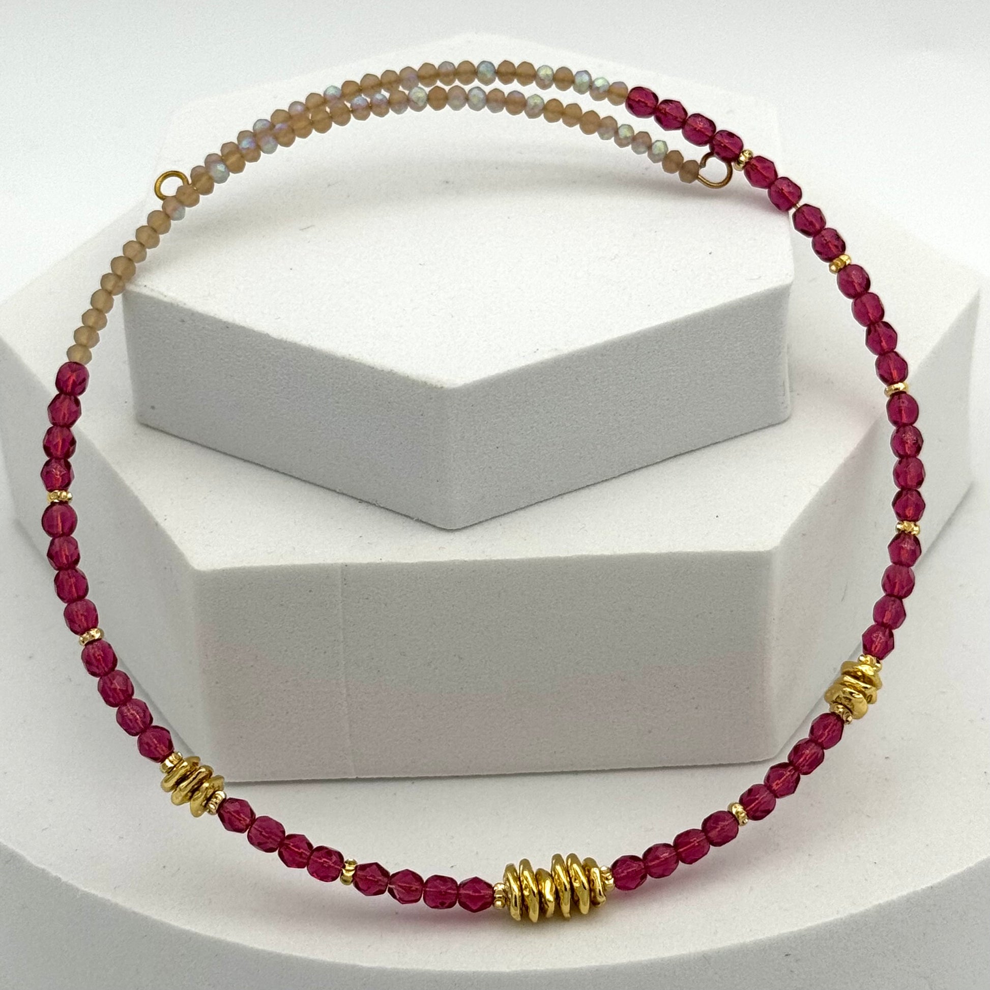 Necklace with red beads and gold accents on a white stand