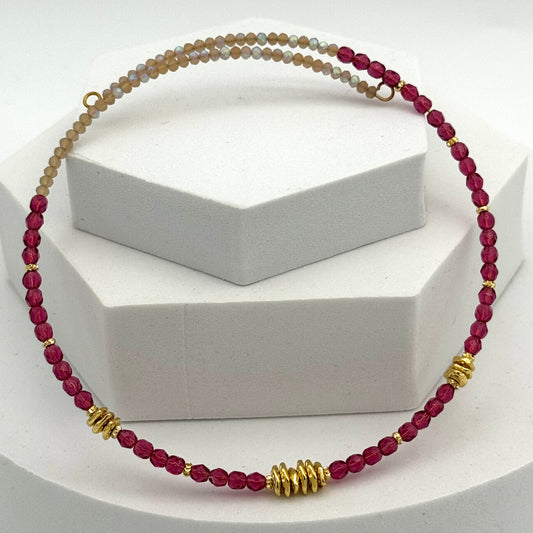 Necklace with red beads and gold accents on a white stand