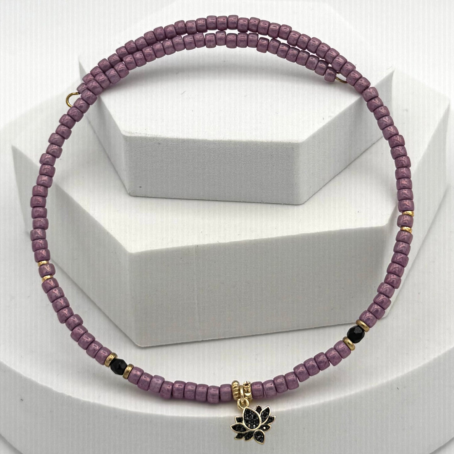 Purple beaded necklace with a black lotus charm on a white background