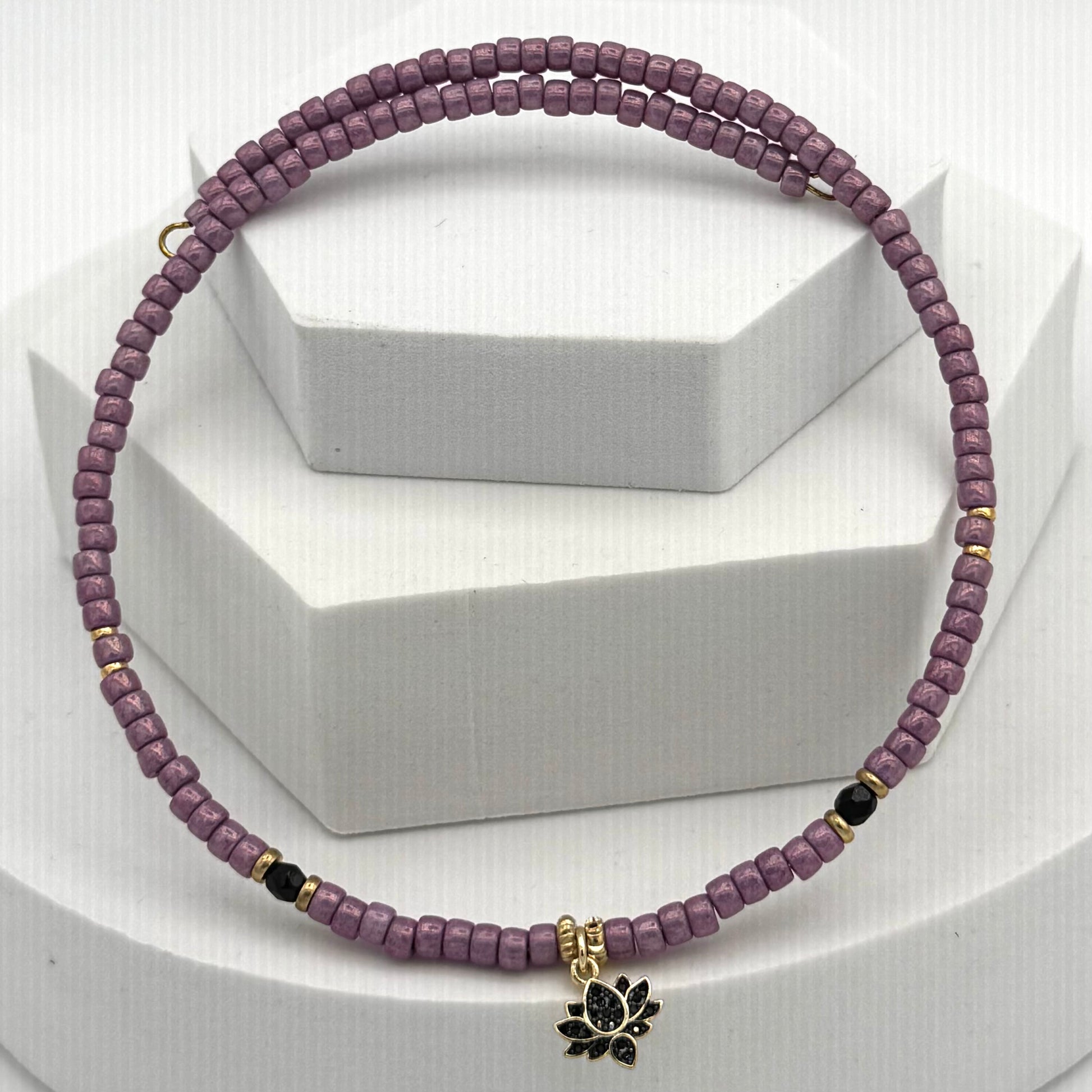Purple beaded necklace with a black lotus charm on a white background