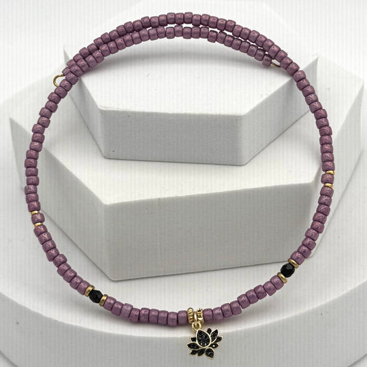Purple beaded necklace with a black lotus charm on a white background