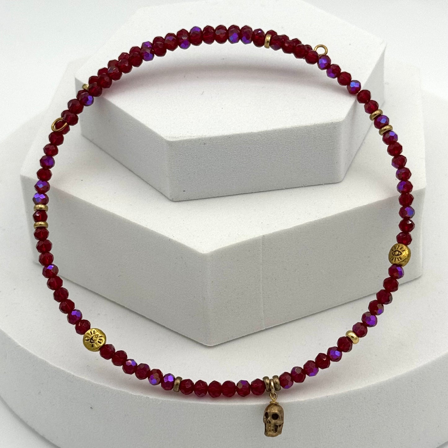 Beaded necklace with red and purple beads and gold accents on a white stand.