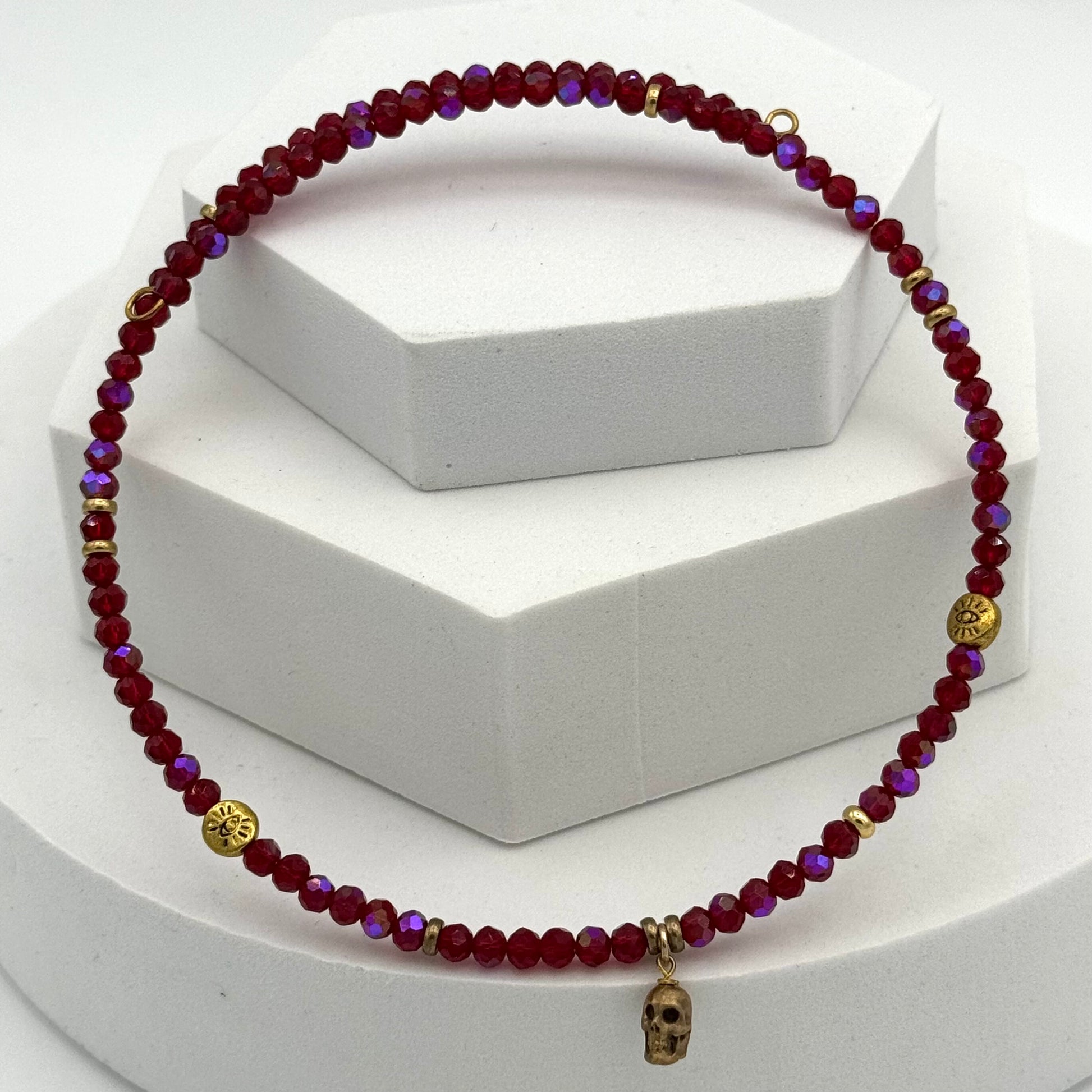 Beaded necklace with red and purple beads and gold accents on a white stand.