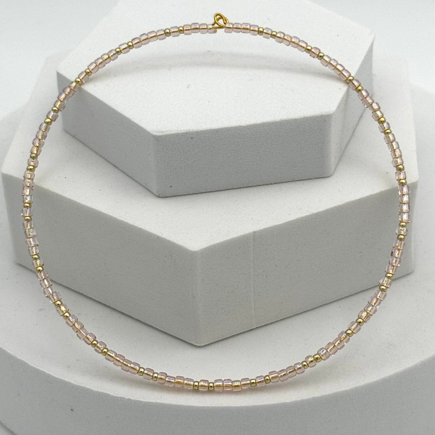Gold beaded necklace on a white hexagonal stand