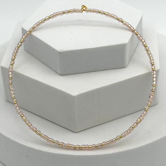 Gold beaded necklace on a white hexagonal stand