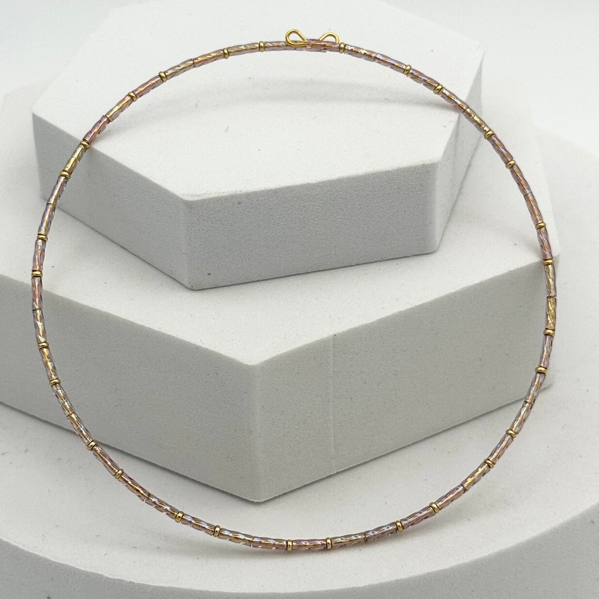 Gold and silver beaded necklace on a white hexagonal stand