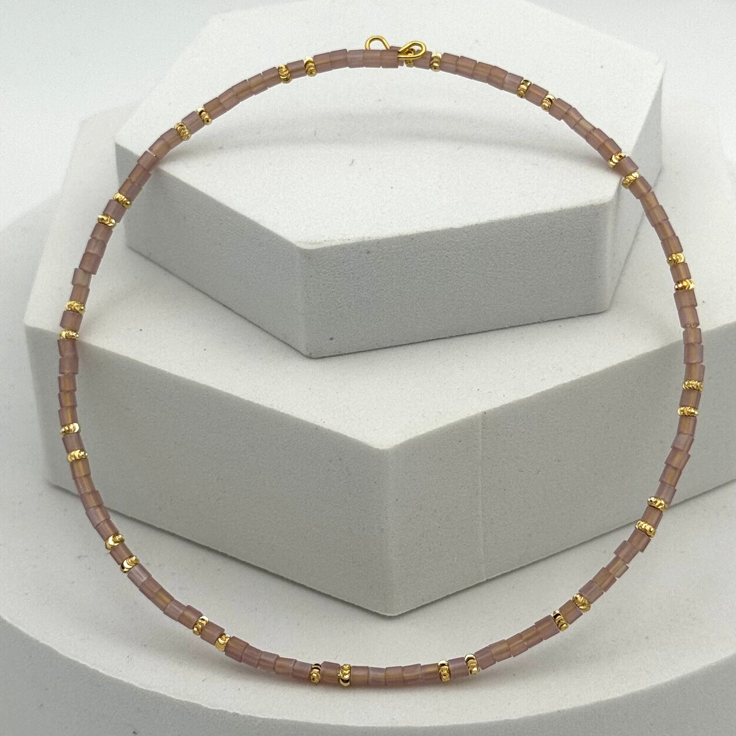 Necklace with brown beads and gold accents on a white stand