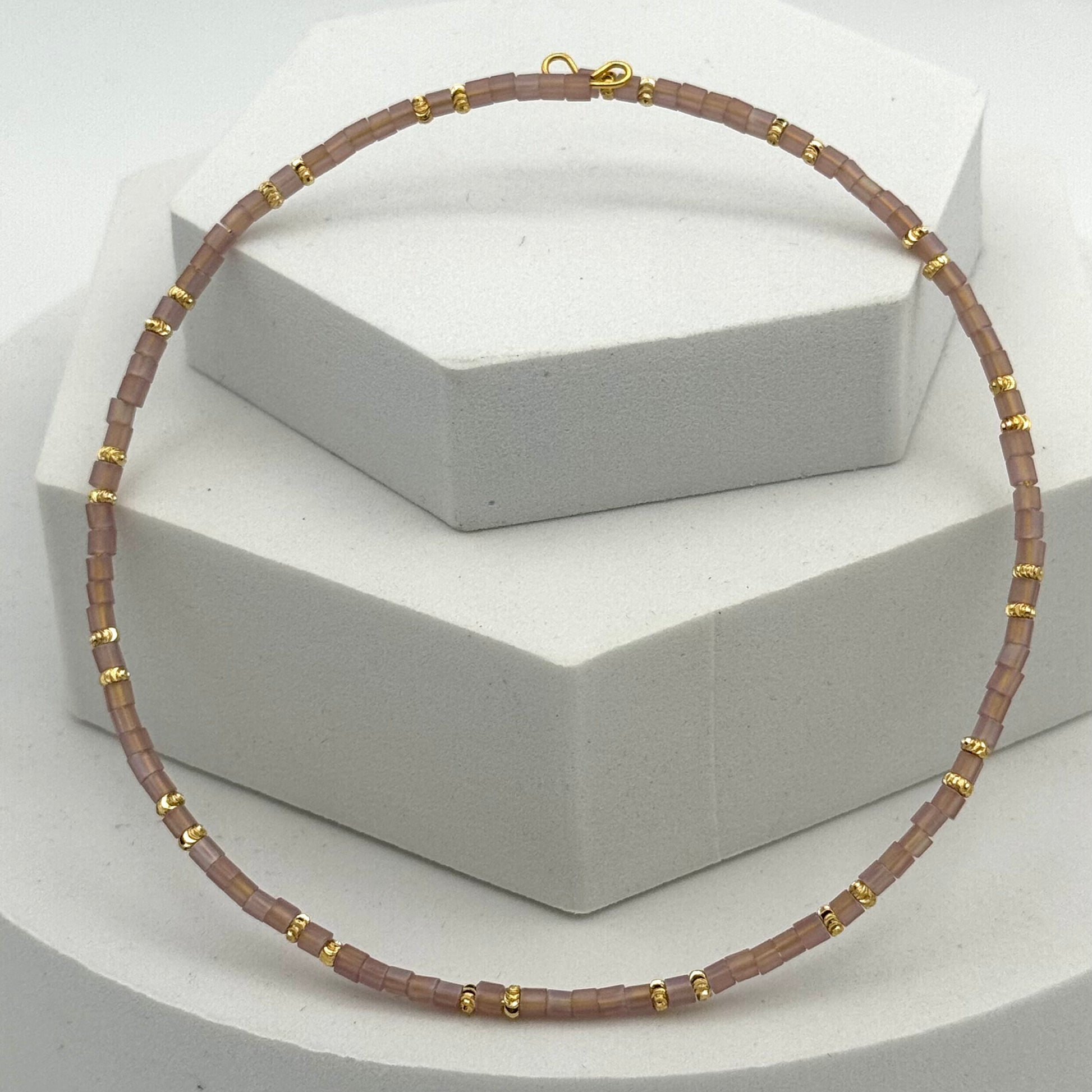 Necklace with brown beads and gold accents on a white stand