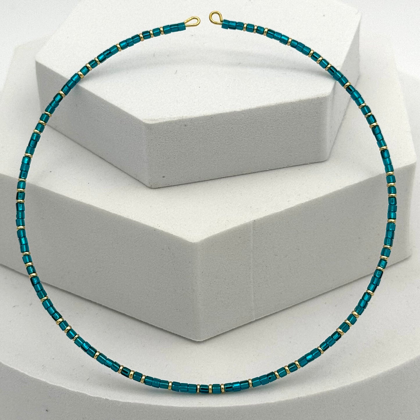 Teal beaded necklace with gold accents on a white stand