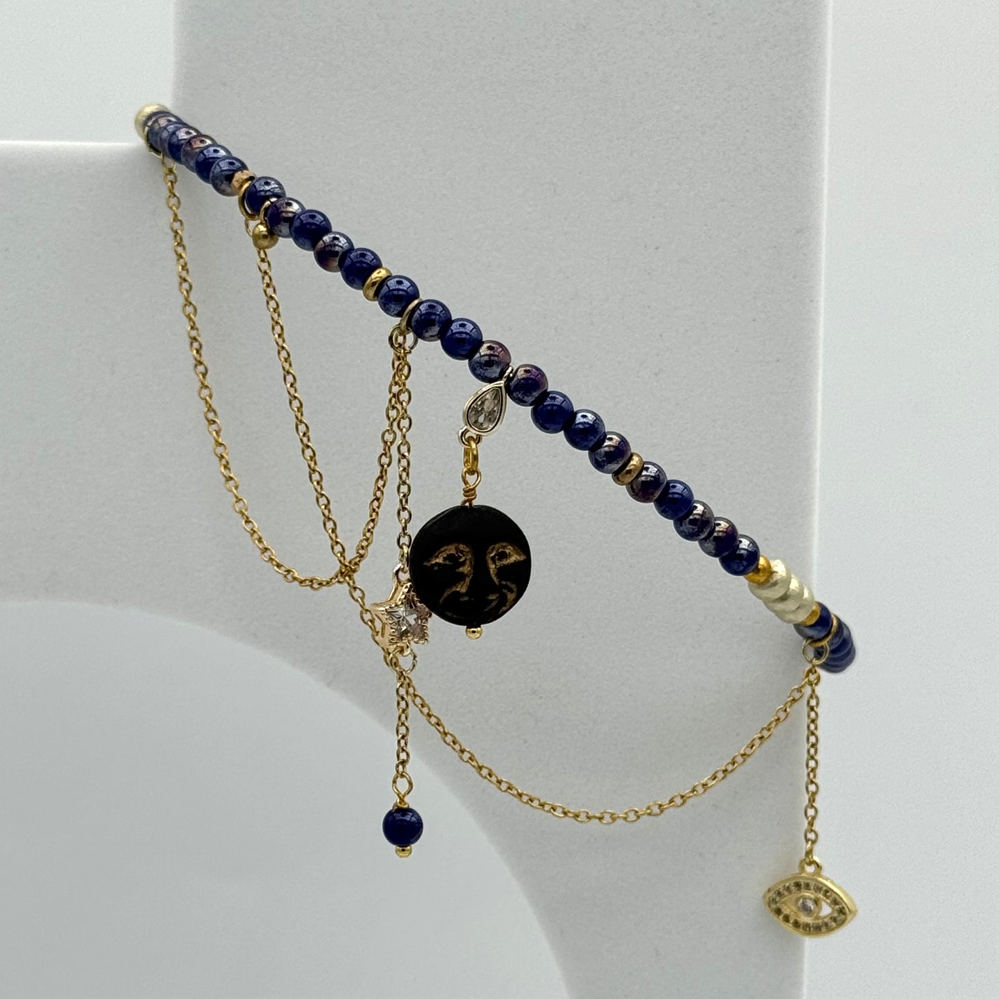 Necklace with blue beads and gold chain on a white stand