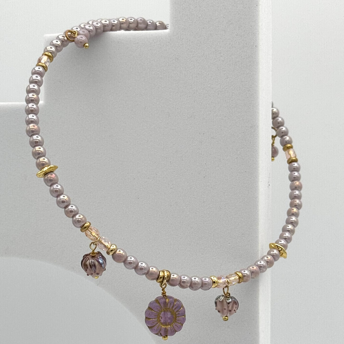 Pearl necklace with gold accents and purple charms on a white background